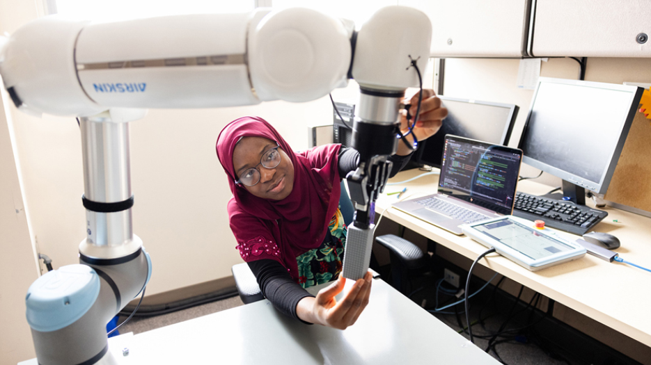 Black female student adjusting a robotic arm used in rehabilitation.